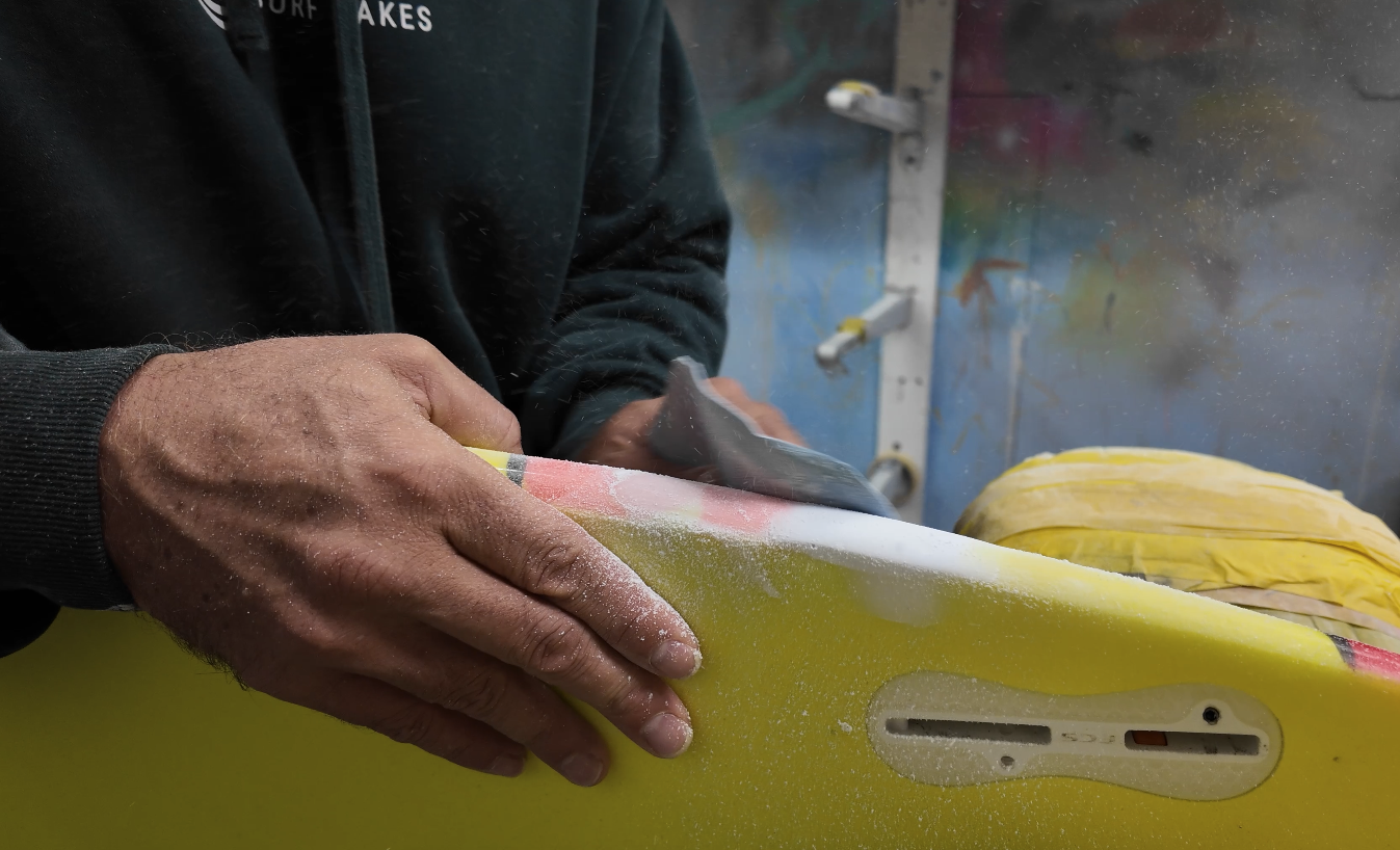 Hand sanding a fresh fibreglass repair on the rail of a yellow surfboard